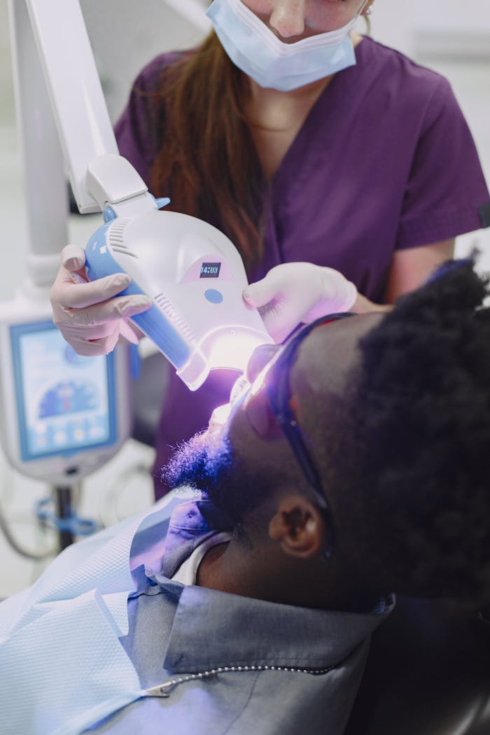 A dental professional applies a curing light to a patients teeth during a whitening procedure.