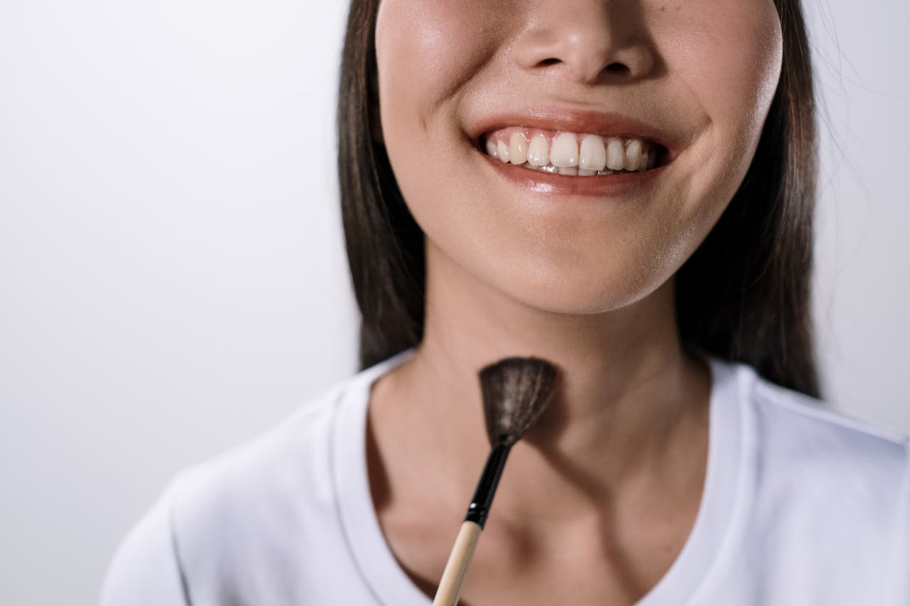 A smiling woman using a makeup brush in a studio on a white background.
